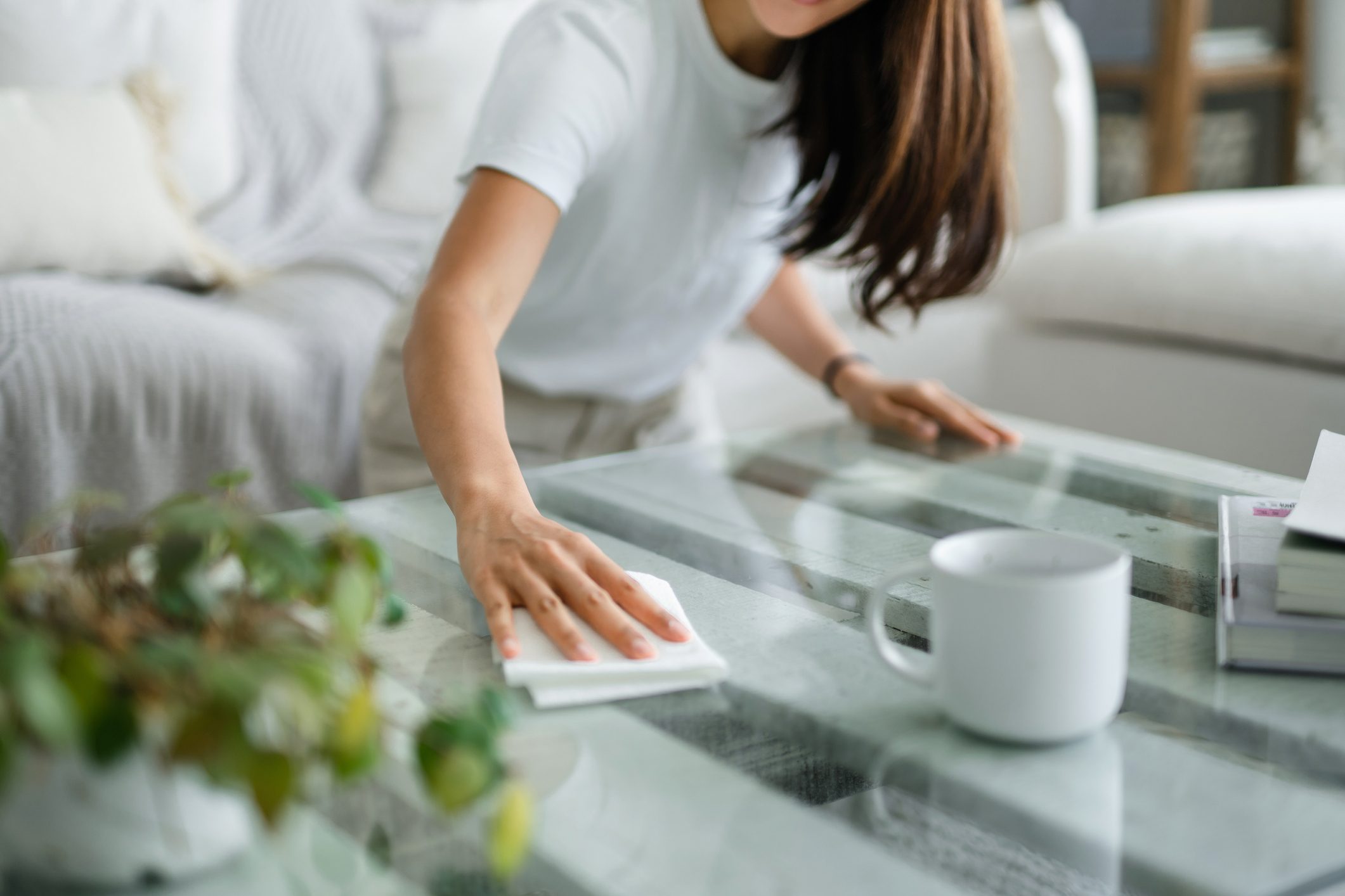Cropped shot of woman tidying up the living room and wiping the coffee table surface with a cloth in apartment living room