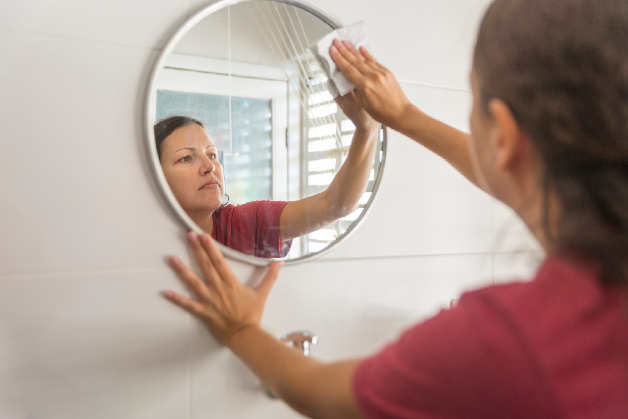 woman cleaning round mirror in small apartment bathroom