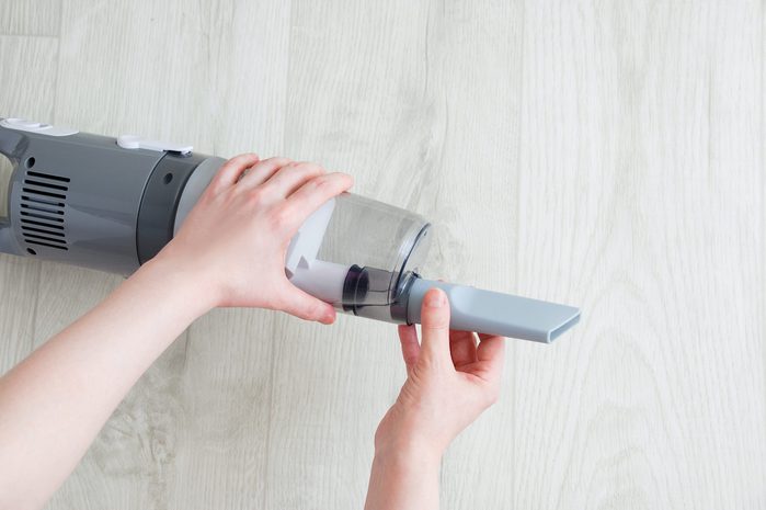 Caucasian woman's hand putting on small crevice tool gray vacuum cleaner on white wooden background.