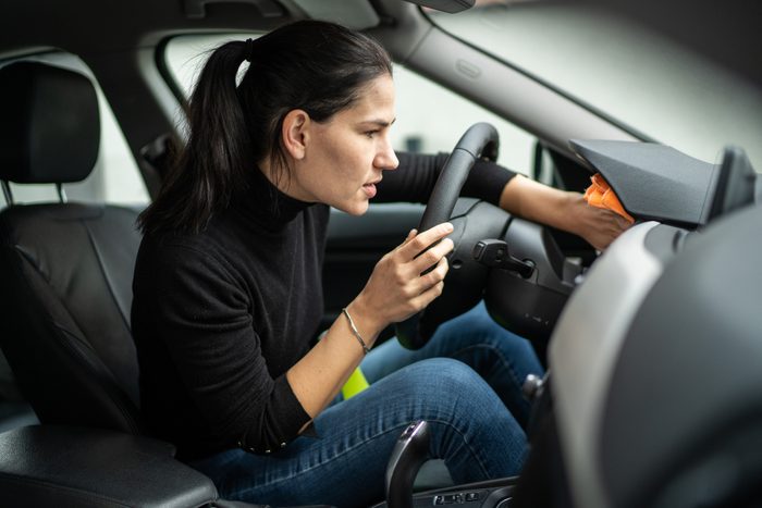 Woman sitting in car and cleaning dashboard with rag