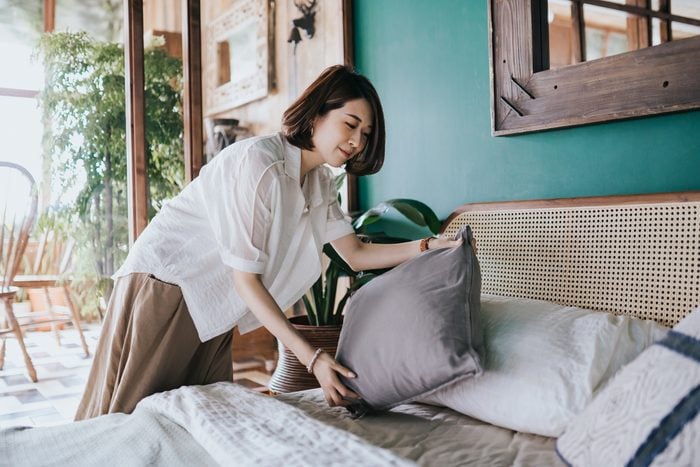 Young Asian woman doing her morning routine, arranging pillows and making up her bed at home. Let's get the day started