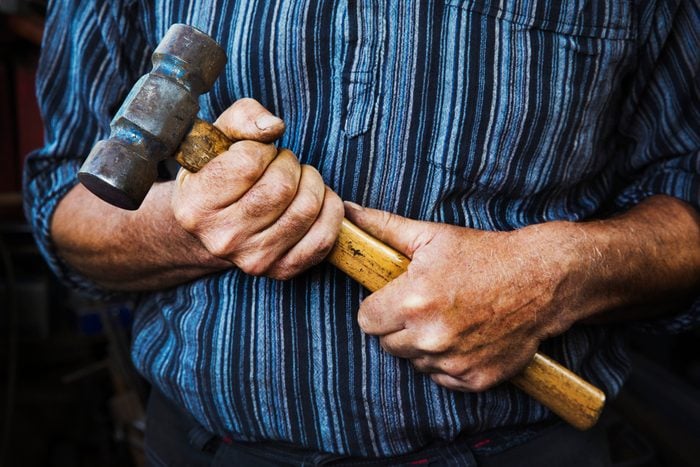 Close up of blacksmiths hands gripping a large hammer.