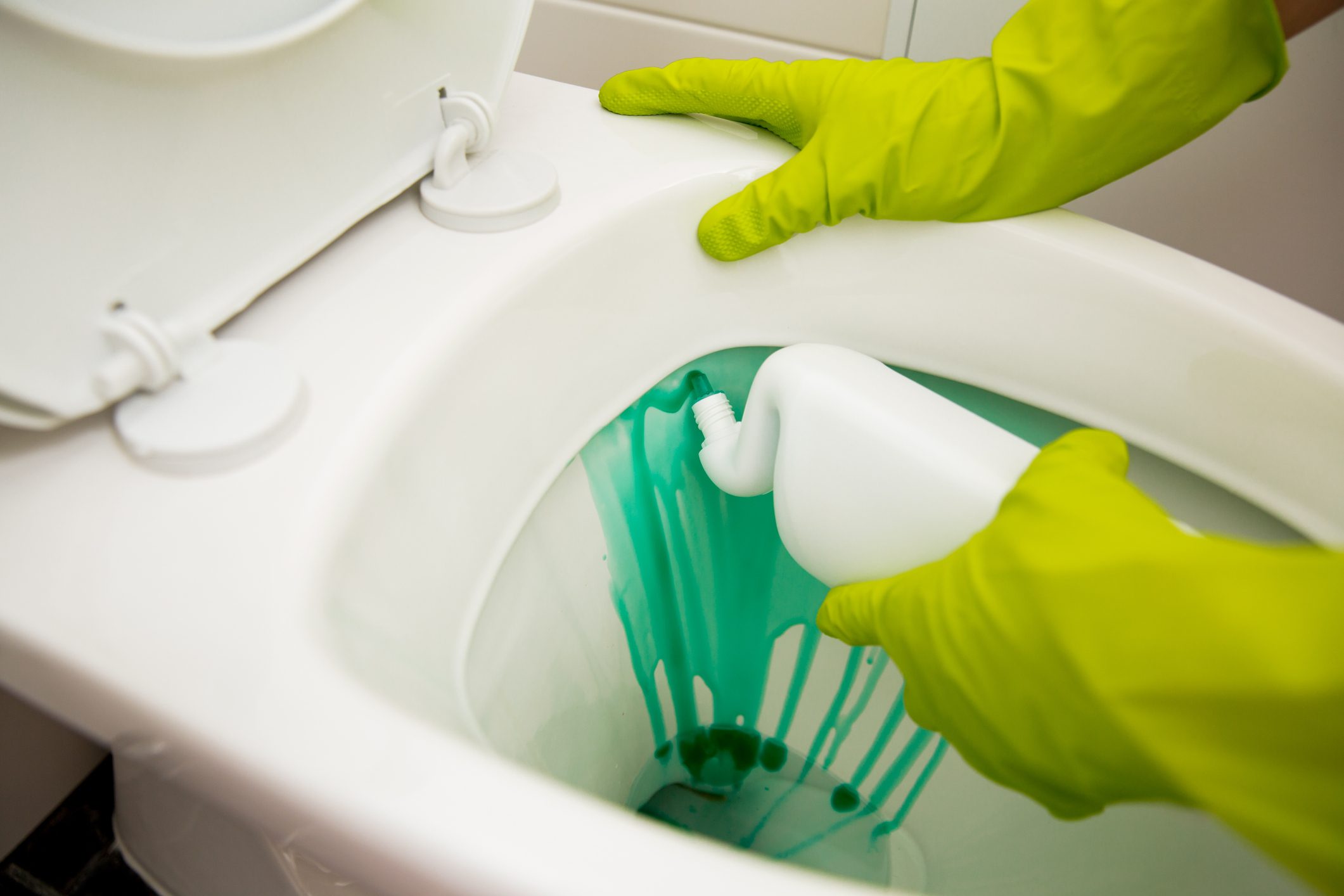 hands in rubber protective gloves adding toilet bowl cleaner to toilet in apartment bathroom