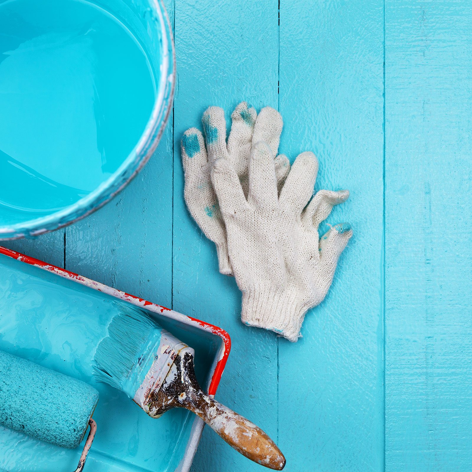 Paint Brush In Teal Blue Color Tray And Paint Bucket, glove On Blue Wooden Background