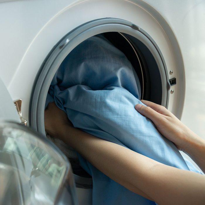 Woman Loads Washer Open Door In Washing Machine With Blue Bed Sheets Inside Close Up