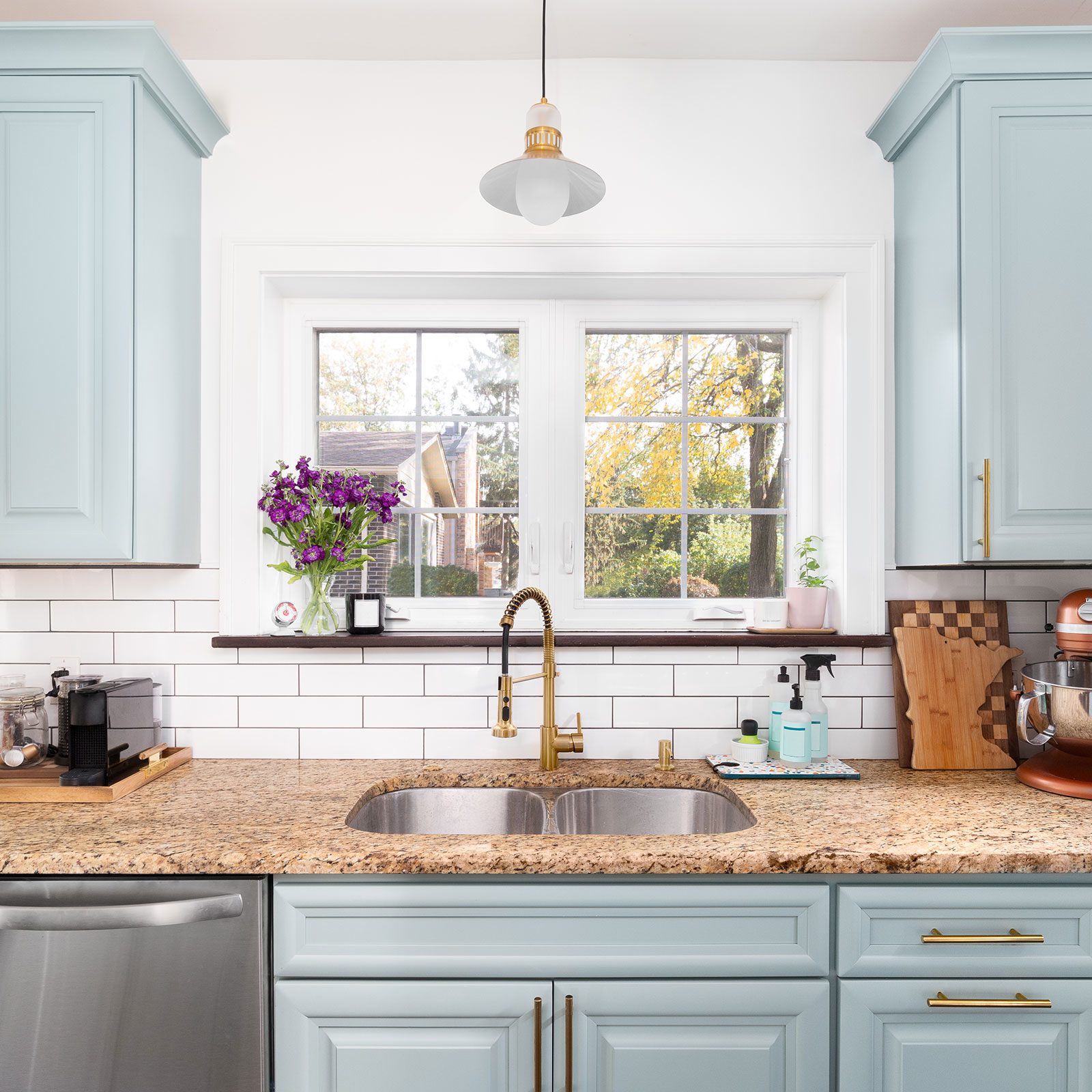 A Light Blue Kitchen With A Gold Faucet And white subway tiles and stainless steel appliances