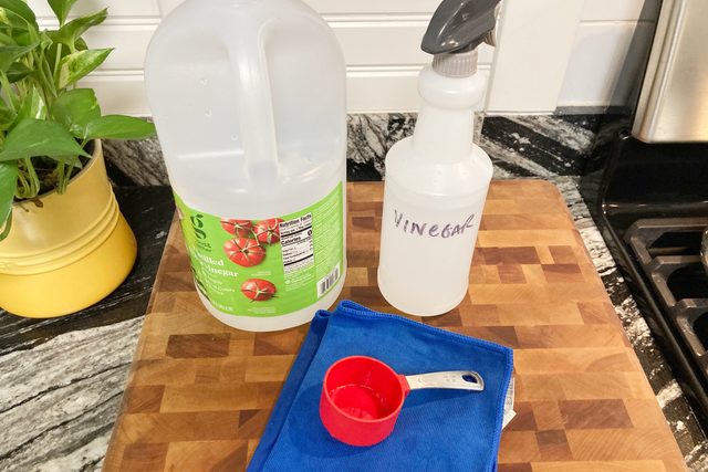 Vinegar, spray bottle, measuring cup and microfiber cloth