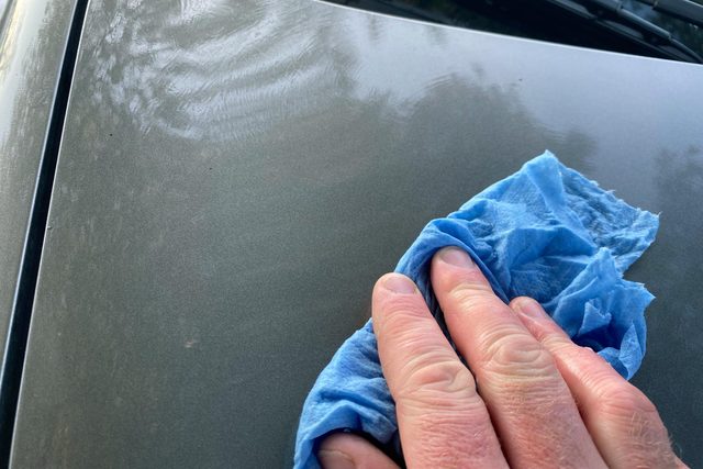 a hand with a blue rag on the hood of a clean car