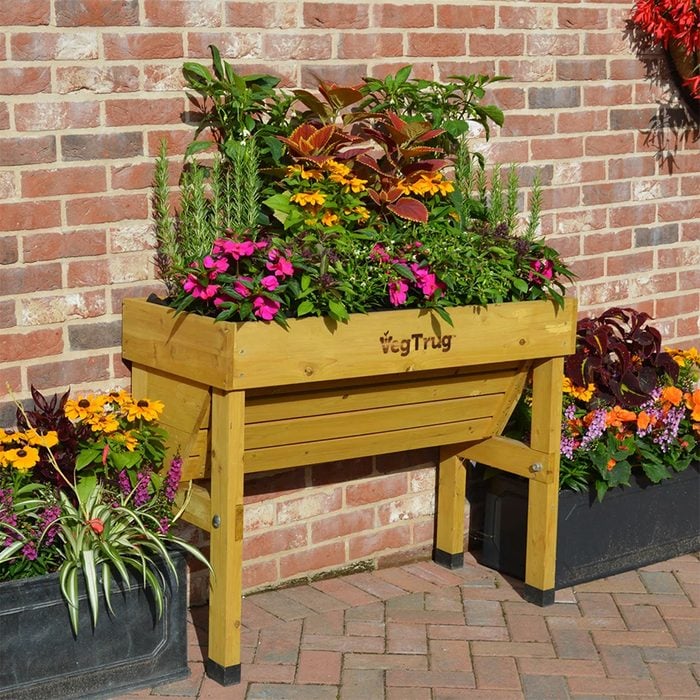 Wood Elevated Planter with flowers outside against a brick wall