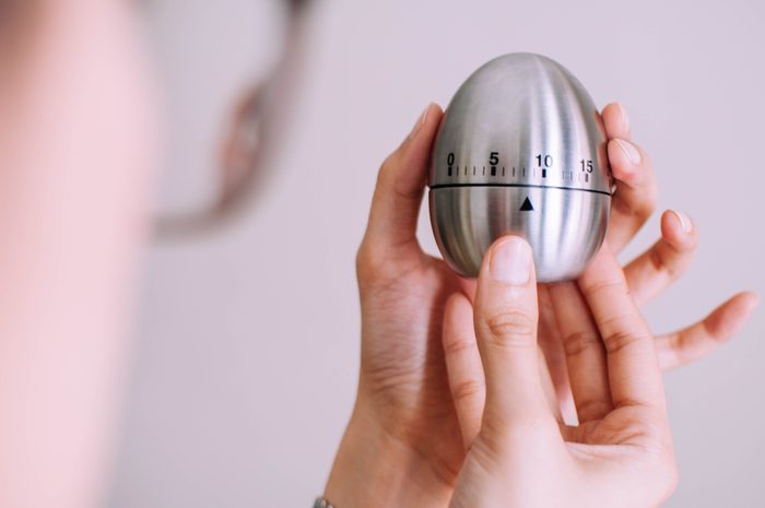 A young woman is holding a metal kitchen egg timer
