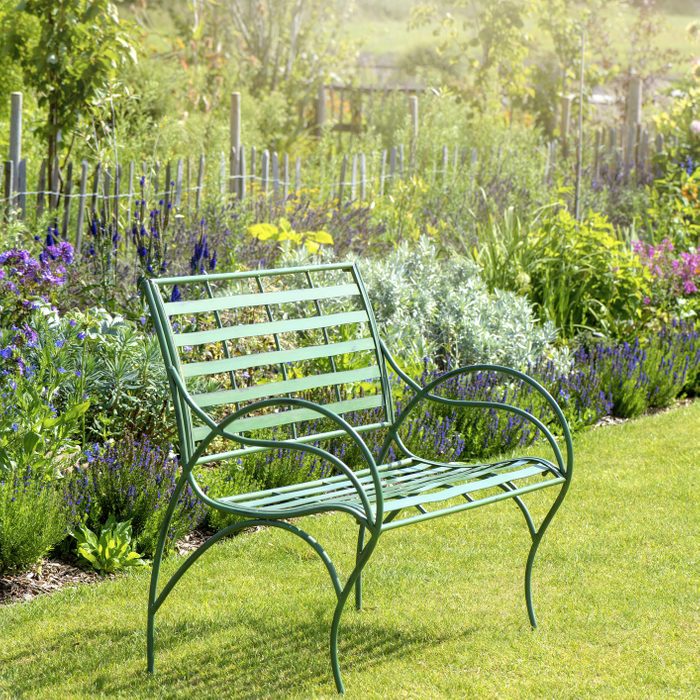 Close-up image of a wrought iron, green garden seat by a summer herbaceous border