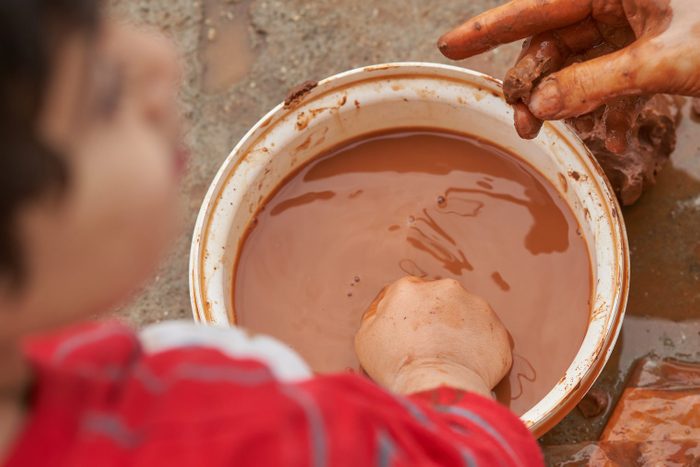 child dips his hand in dirt and water mixture