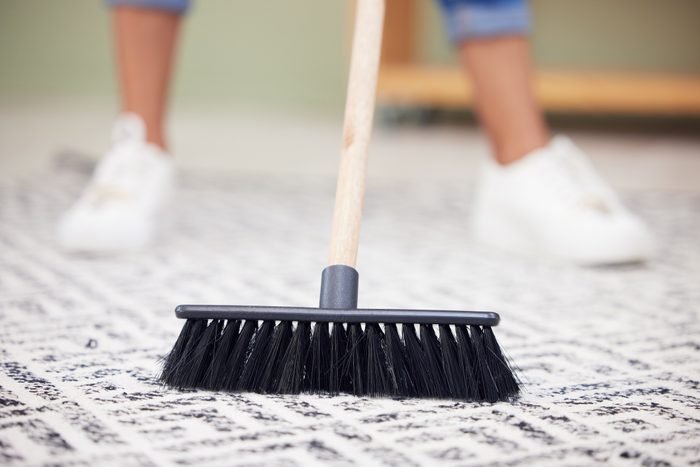 Cropped shot of an unrecognizable woman sweeping the carpet at home