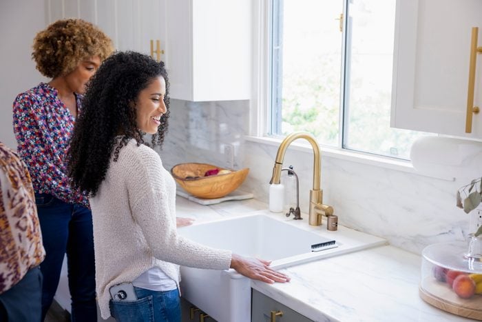 Smiling young woman touching kitchen sink while discussing with female real estate agent