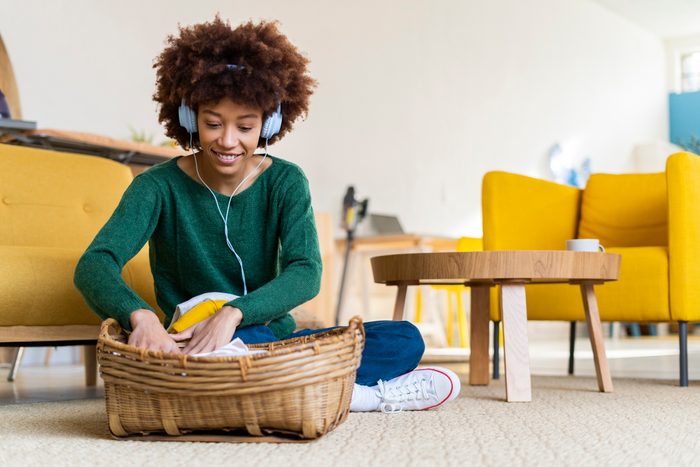 Young Afro woman listening music sitting cross-legged by basket in living room
