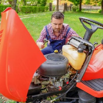 One gardener mowing grass fixing lawn mower engine problem