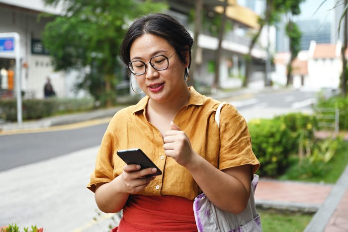Asian woman walking down the street looking at her phone and checking her credit score