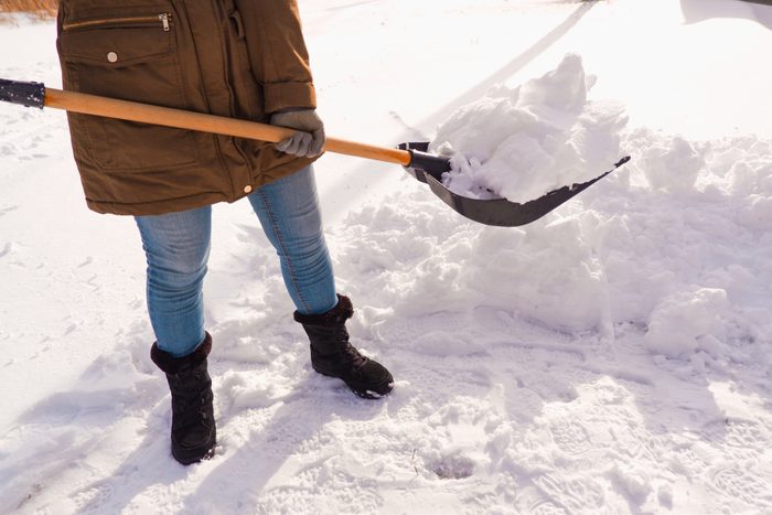 Snow removal in winter. A woman cleans the snow with a shovel in the local area. Woman clearing snow from her front yard.