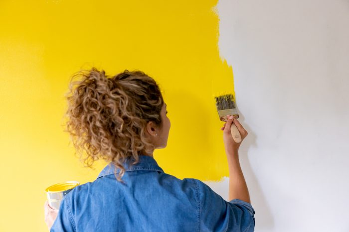 Woman at home painting a wall yellow