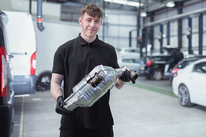 Apprentice Mechanic Engineer Holding Catalytic Converter In Car Service Center