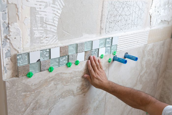 Tile Border made up of small square glass tiles are adhered to the wall by a tile installation worker