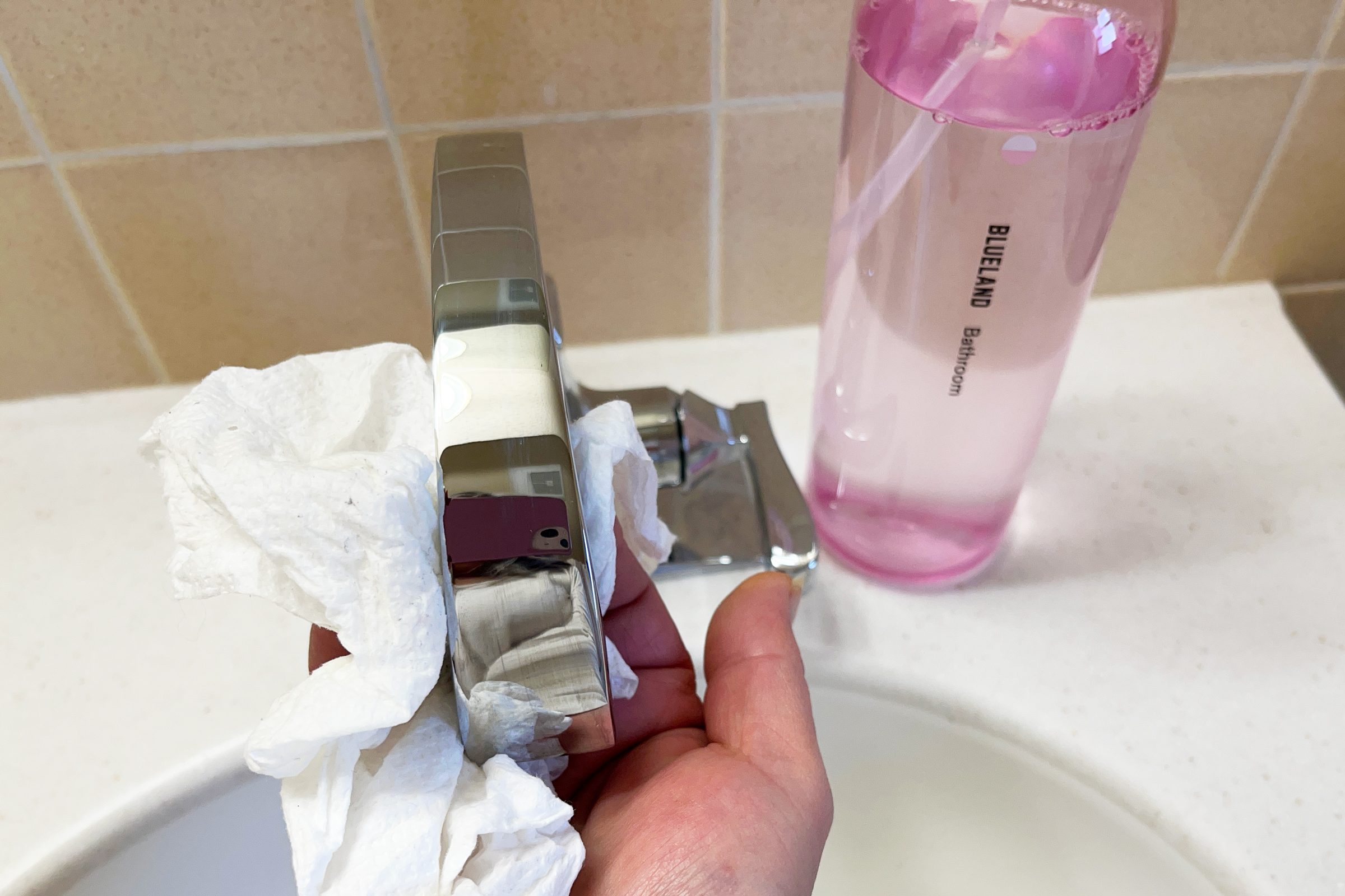 hand cleaning a bathroom sink faucet with a pink bottle from the Blueland Cleaning Kit