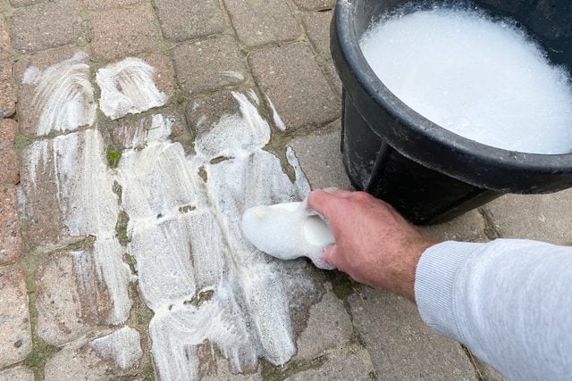 hand washing pavers with a bucket of soap and water and a sponge