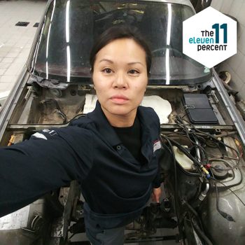 selfie of Nhu Nguyen working on restoring a car with the eleven percent logo in the corner