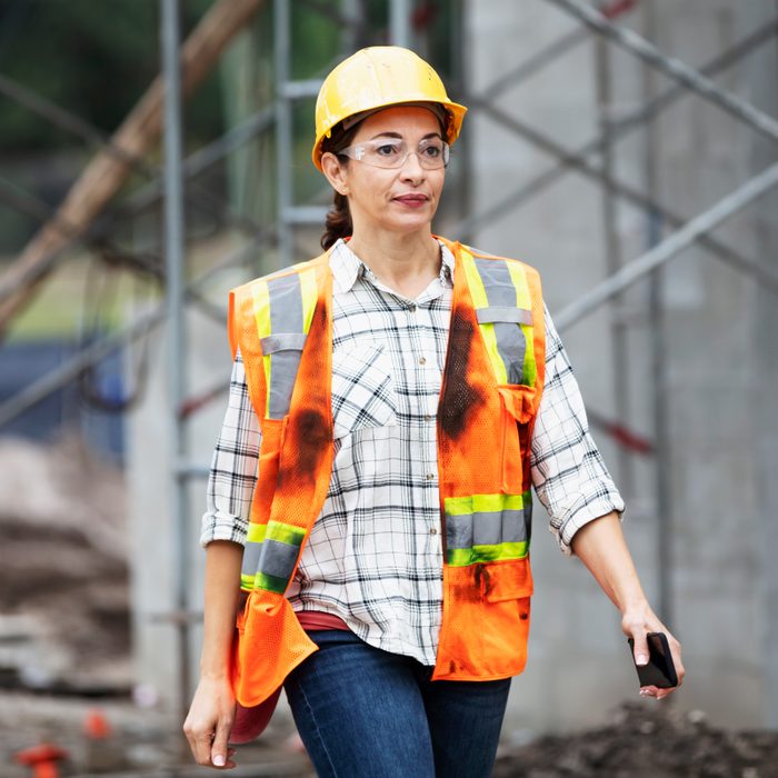 construction woman wearing an orange vest, hard hat and safety glasses