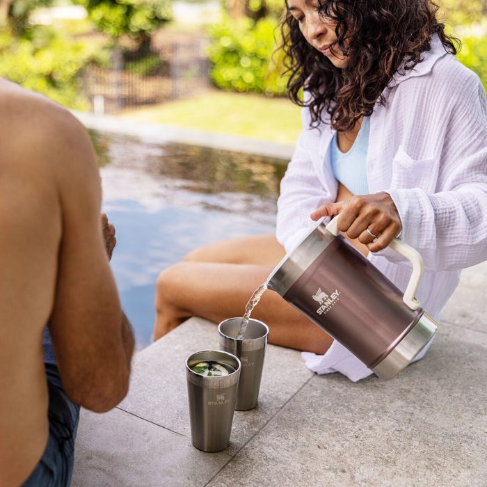 woman sitting by the pool pouring a drink from a Stanley pitcher into two Stanley beer pints