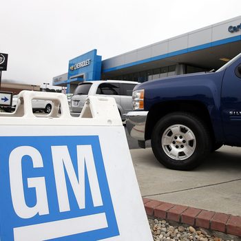 GM Sign Logo sits in front of A brand new Chevrolet truck is displayed at a Chevrolet dealership