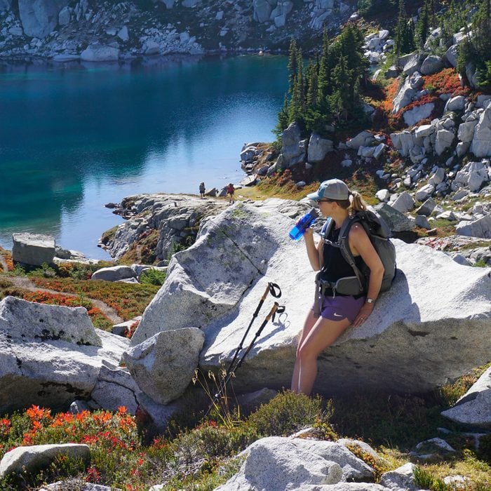 woman drinking from a water filter bottle by a lake and mountains