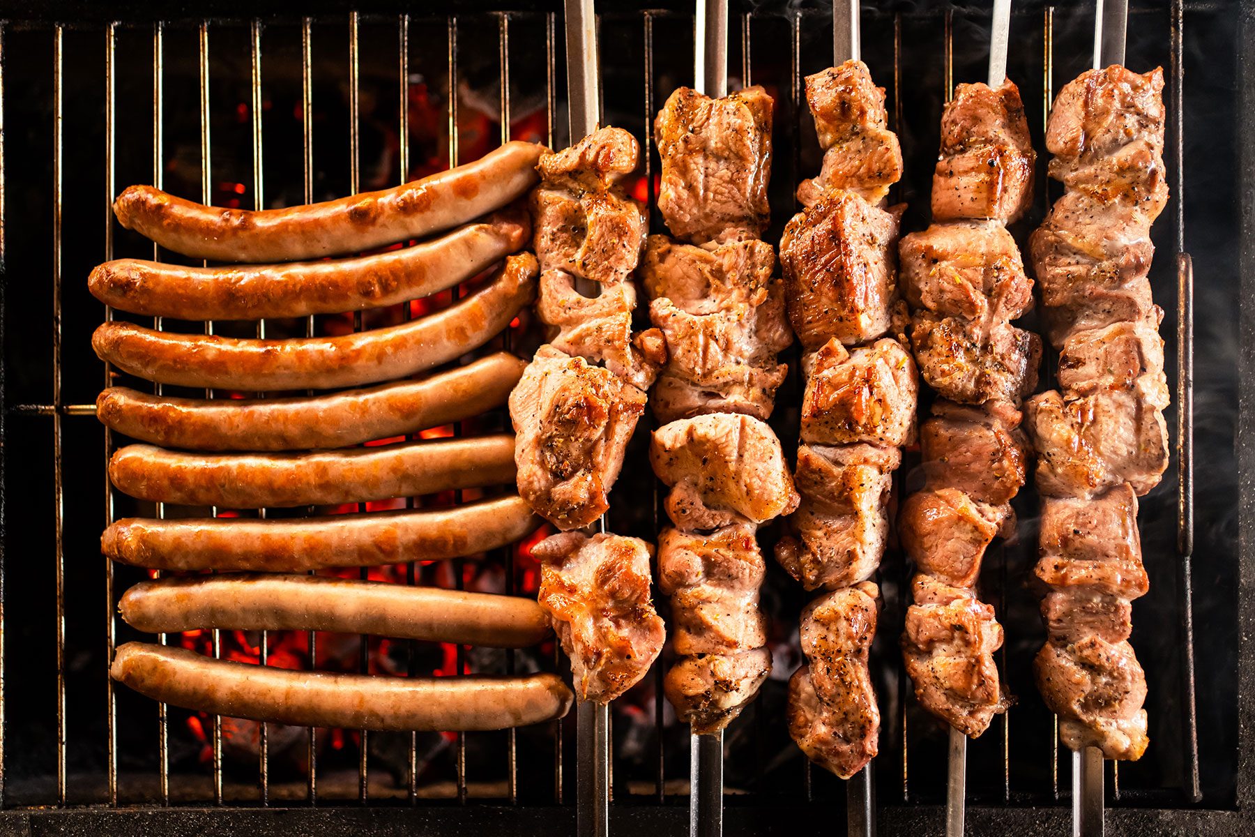 Meat On Skewers And Sausages Are Cooking On The Grill