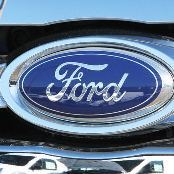 Ford Logo and Cars are reflected off of the grill of a new ford truck at a car dealership