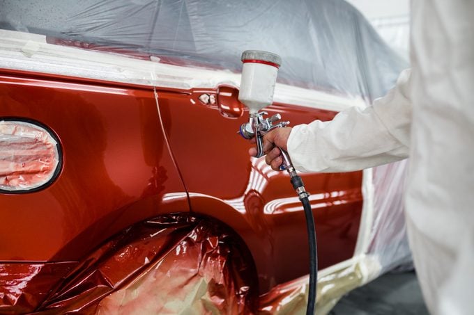 Man with protective clothes and mask painting car using spray compressor.