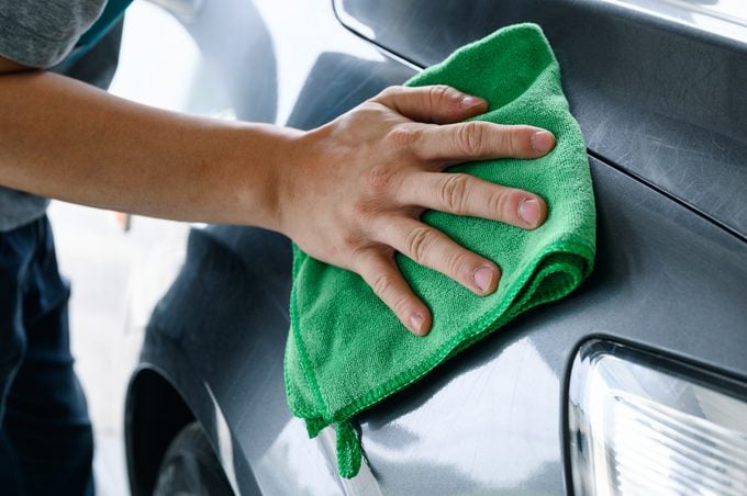 Man cleaning car with green microfiber cloth on hood