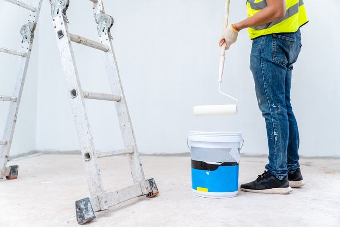 Painter man painting the wall, with paint roller and bucket in an unfinished house, Construction work, isolated on big empty space with ladder