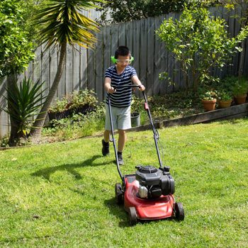 Teenage boy wearing headphones mowing lawn in backyard