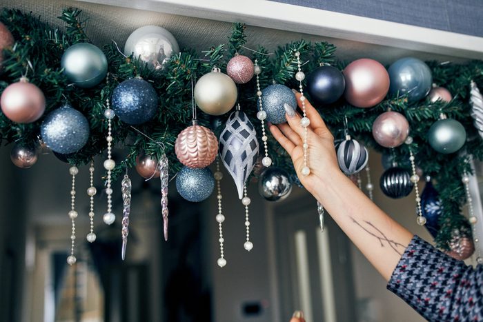 Decoration of the apartment for Christmas and New year. A woman decorates the doorway with spruce branches and Christmas tree toys