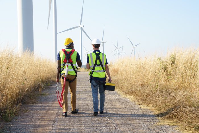 Back view of wind turbine workers discussing work at wind farm energy