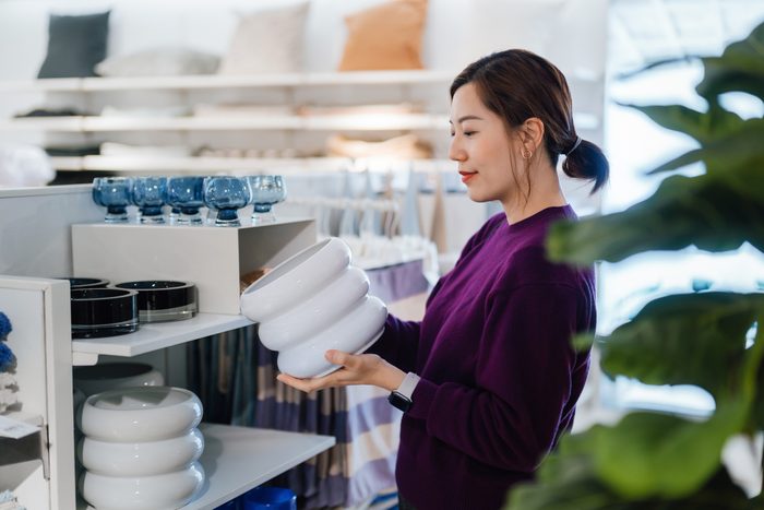 Young Asian woman shopping for home decor and household necessities in a homeware store, looking at a ceramic vase on a shelf