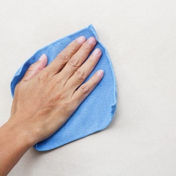 hand using a blue microfiber cloth the clean a white wall