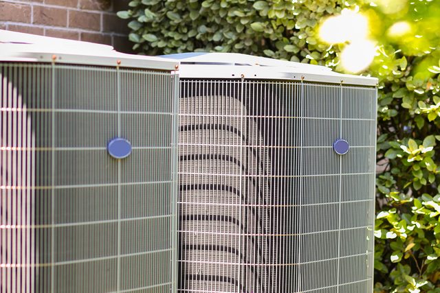 Home Air conditioner unit outdoors in side yard of a brick home in hot summer season