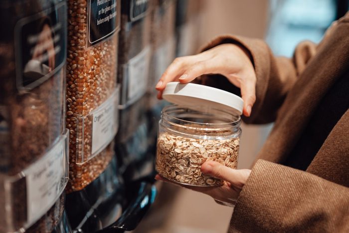 Woman in organic whole foods refilling store dispensing oats into a reusable container.