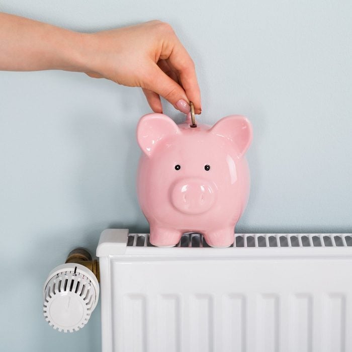 Woman Hand Inserting Coin In Piggybank On Radiator