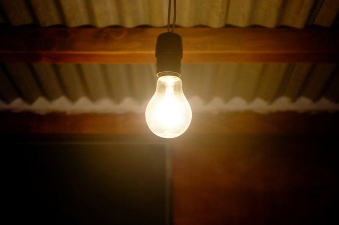 An old incandescent bulb plugged in and glowing in an outdoor porch light socket