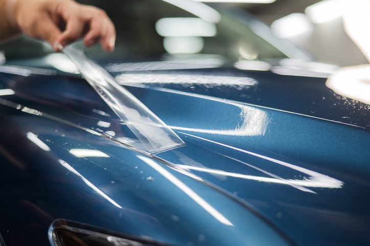 The master in the car service applies a protective armor film to the car body.