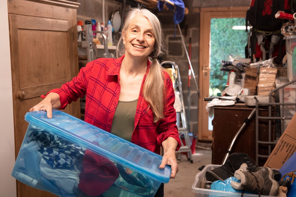 A mature woman smiles as she carries boxes of belongings to sort through whilst in lockdown at home.