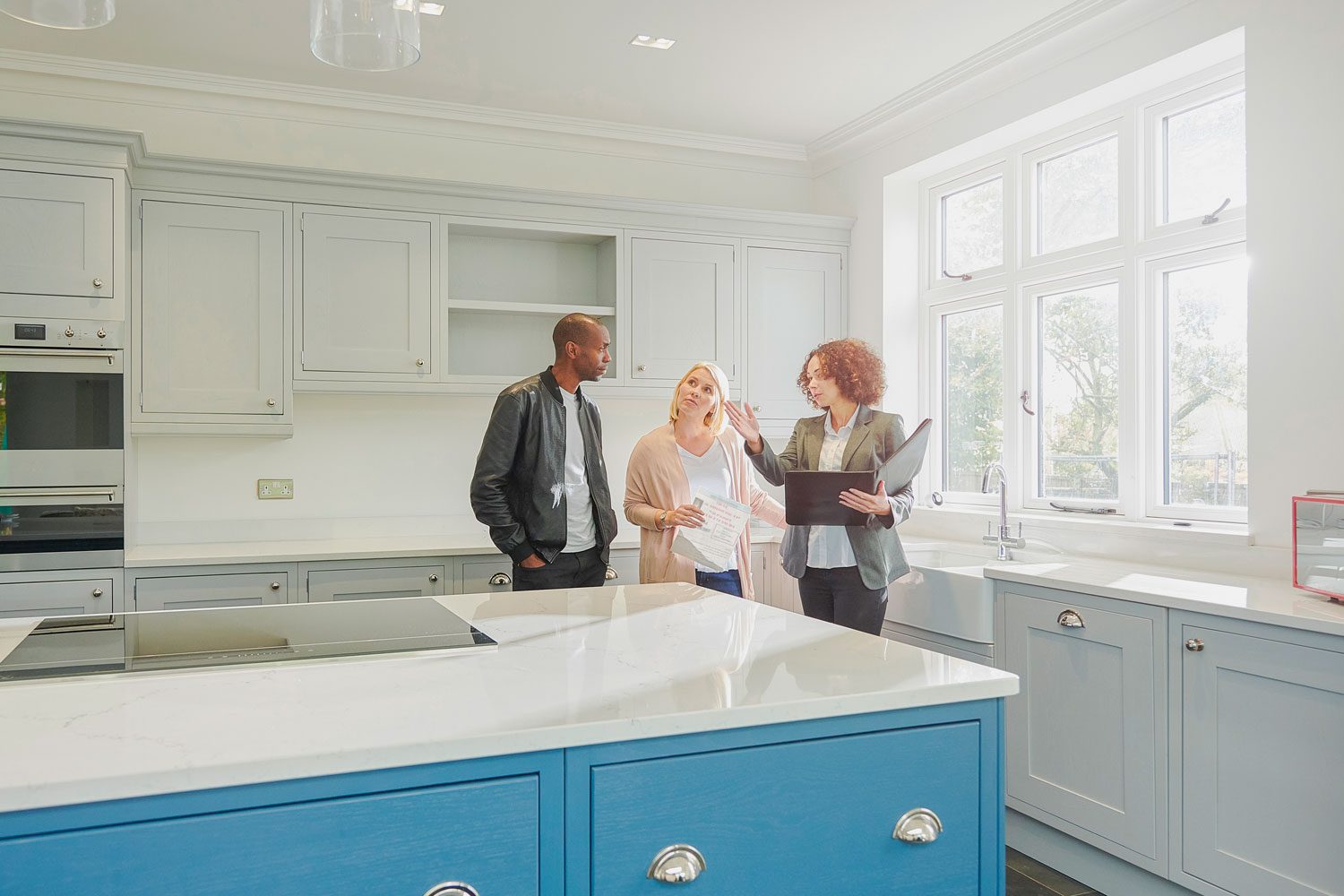 a saleswoman or estate agent shows a couple around a home with new kitchen