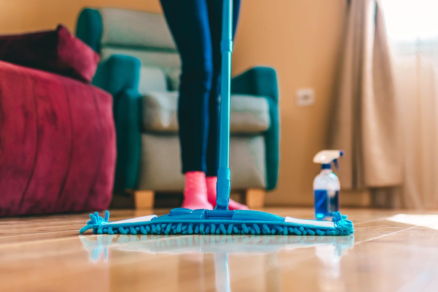 Young Woman Mopping Hardwood Floors with a Sponge Mop and Cleaning Supplies in the Background